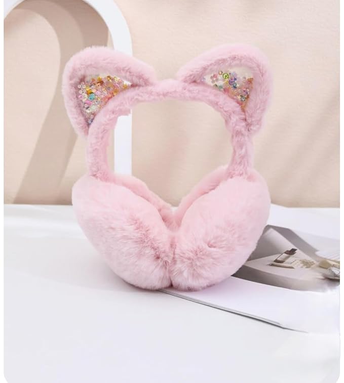 The image shows a pair of pink, fluffy earmuffs with cat ear designs adorned with colourful glitter accents, placed on a white surface with a subtle background featuring an arch and some papers.
