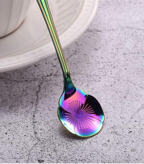 A colourful, iridescent spoon with a unique starburst pattern on the bowl rests on a white plate, set against a textured grey surface.