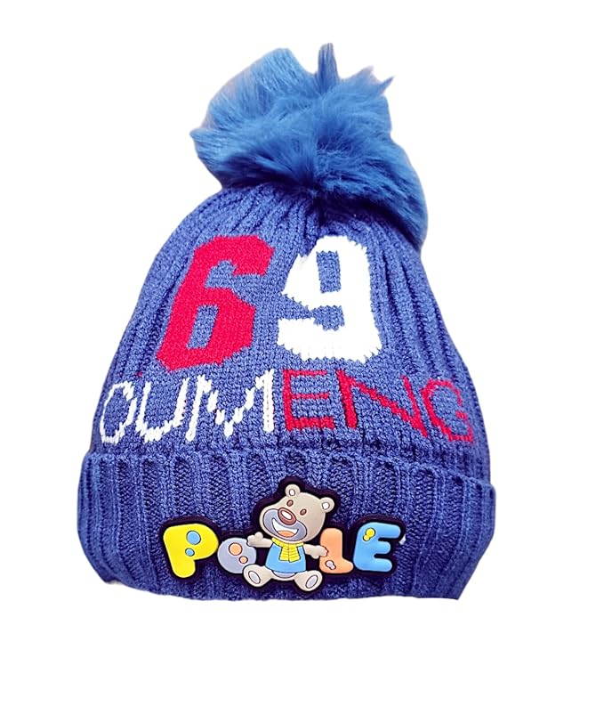 A blue knitted baby hat with a fluffy pom-pom features red "6" and "9", white "OUMENC" text, and a colourful "Pooie" bear patch. Placed on a wooden surface, it’s set against a blurred background with a globe and colourful books, suggesting a kids' room.